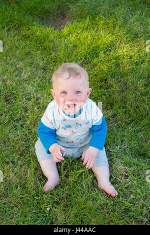 Huit mois baby boy smiling et assis sur l'herbe, dans le sud du Devon, Angleterre, Royaume-Uni. Banque D'Images