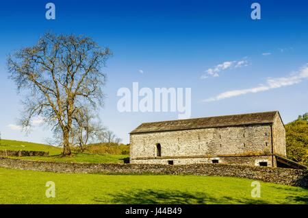 Une grange et tree situé dans la campagne anglaise avec un champ vert au premier plan sous un ciel bleu. Banque D'Images