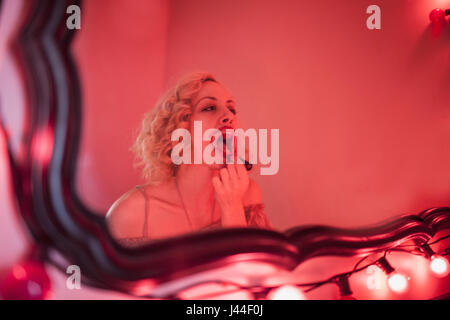 A young woman applying lipstick dans un miroir. Banque D'Images
