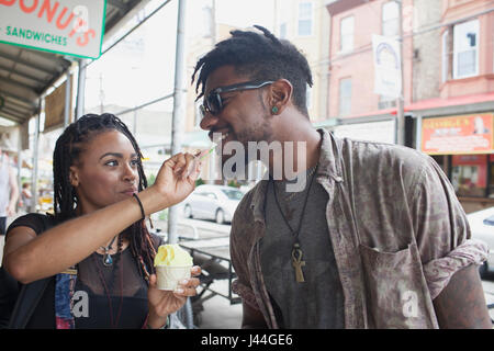Une jeune femme nourrissant un jeune homme du yogourt glacé. Banque D'Images
