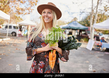 Heureux sain jeune femme de la farmers market holding carrots et kale achetés d'un décrochage Banque D'Images