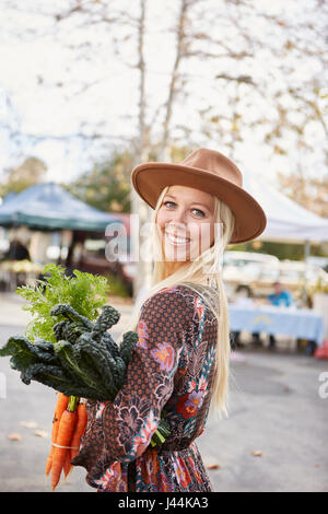 Heureux sain jeune femme de la farmers market holding carrots et kale achetés d'un décrochage Banque D'Images