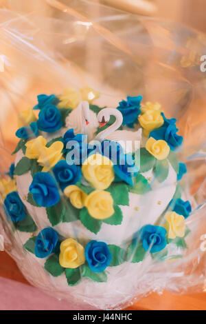 Gâteau de mariage décoré mignon avec glaçage bleu et jaune fleurs, deux figurines de cygnes en haut Banque D'Images