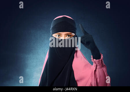 Belle asiatique femme musulmane en voile avec pointage bouleversé les yeux sur un fond sombre Banque D'Images