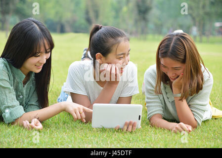 Trois jolies filles, se trouvent exposés sur l'herbe.Utiliser la tablette Banque D'Images