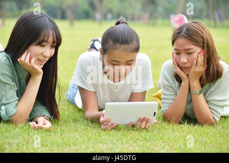 Trois jolies filles, se trouvent exposés sur l'herbe.Utiliser la tablette Banque D'Images