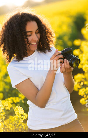 Beautiful happy mixed race African American girl adolescent femme jeune femme smiling outdoors dans sunshine de prendre des photographies avec un appareil photo Banque D'Images