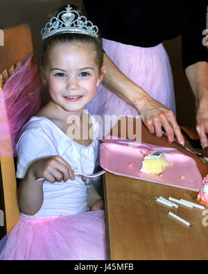 Belle petite fille est en compagnie de ses ballerines d'anniversaire. Elle porte une couronne et tutu rose. sa fourchette est prêt à manger sa tranche de c Banque D'Images