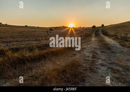 Un coucher de soleil en Toscane, avec le soleil qui descend derrière une colline, avec haybales et un sentier de randonnée à venir Banque D'Images