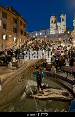 Place d'Espagne à Rome un touriste posant pour une photo de la fontaine de l'affreux voile de soirée, la nuit avec le fond de l'église Trinità dei Monti. Banque D'Images