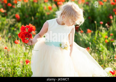 Kids Fashion, petite fille, printemps, mariage, enfance heureuse concept - belle petite blonde kid wearing white dress avec bouquet de fleurs dans les champs de coquelicots Banque D'Images