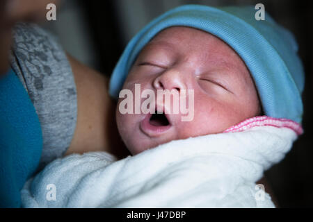 Stock photo ID : 534685885 un bébé nouveau-né garçon enveloppé dans une couverture blanche et chapeau tricoté bleu dort dans les bras de sa mère avec la bouche ouverte et les yeux fermés Banque D'Images