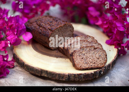 Bananes en tranches de pain fait maison de noyer et affichée sur une planche à découper de grain de bois entouré de fleurs de bougainvilliers roses Banque D'Images