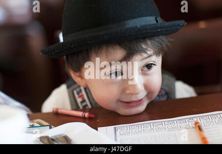 Cute little young asian woman avec joues potelées portant un chapeau fedora noir s'appuyant son menton sur une table avec des crayons crayola autour de lui Banque D'Images