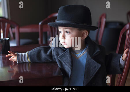 Cute Young Asian Woman petit garçon vêtu d'un pull bleu et gris à pois noir avec une fedora regarde par la fenêtre dans la matinée d'hiver Banque D'Images