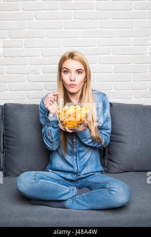 Young woman watching TV and eating chips Banque D'Images