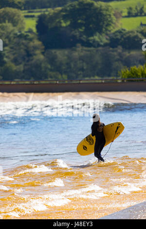 Un surfeur holding surf board à la piscine à vagues artificielles dans la vallée de Conwy sait aussi surfer sur Snowdonia, avec l'hébergement glamping chalets Banque D'Images