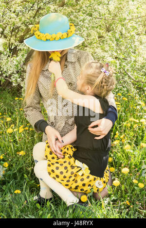 Fille est assise sur les mains à la mère et lui offre un bouquet de pissenlits sniff Banque D'Images