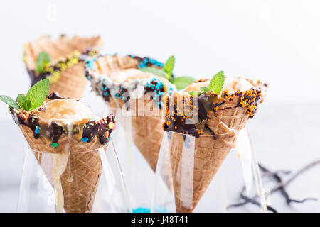 Glace vanille avec sauce au caramel en cornet gaufré décoré de chocolat noir et de Nutrifer servi en verre sur table gris clair Banque D'Images