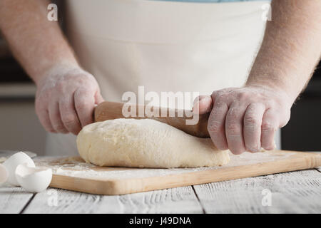 Chef cuisinier homme ou pelmeni Knedlík ou raviolis dans une moule. Aplatir la pâte avec un rouleau à pâtisserie sur la table rustique, vue avant Banque D'Images
