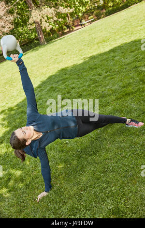 Femme avec kettlebell faisant du yoga au parc Banque D'Images