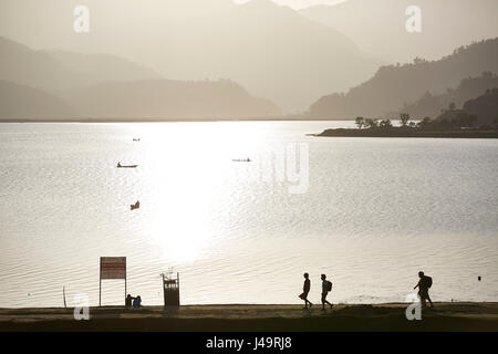 La silhouette des gens marcher sur un chemin par un lac, un lac au coucher du soleil, Pokhara, Népal Banque D'Images