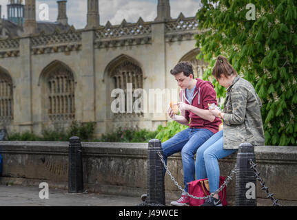 Un couple d'étudiants s'asseoir manger leur repas sur un muret à l'extérieur de l'avant de King's College à l'université de Cambridge, Angleterre, Grande-Bretagne. Banque D'Images