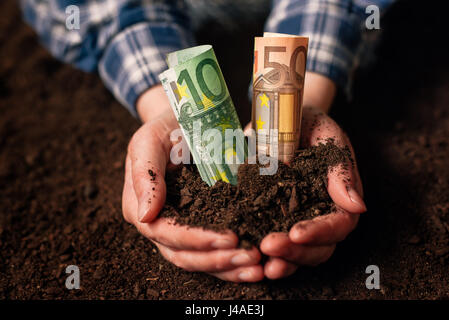Les mains avec un sol fertile et de l'argent euro banknotes, female farmer poignée de terres cultivées qui fait de profit et de revenu régulier de l'aménagement durable d'agricu Banque D'Images