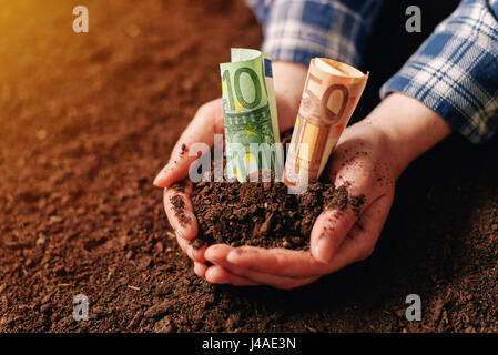 Les mains avec un sol fertile et de l'argent euro banknotes, female farmer poignée de terres cultivées qui fait de profit et de revenu régulier de l'aménagement durable d'agricu Banque D'Images