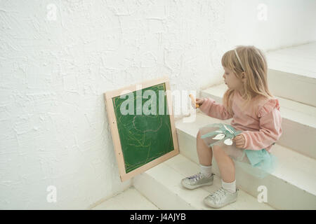 Cute girl en tête d'argent lié écrit sur tableau noir craie, assis Banque D'Images