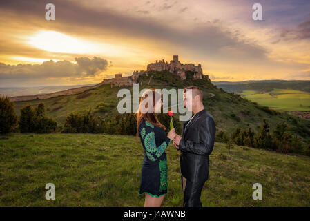 Jeune couple amoureux au coucher du soleil près d'un château en ruines. L'homme est de donner une tulipe rouge à sa petite amie. Banque D'Images