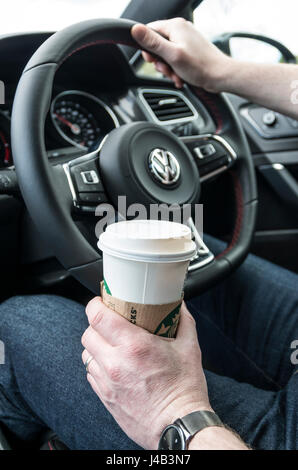 Homme conduisant au volant d'une voiture avec une main sur le volant et une tasse de café dans l'autre Banque D'Images