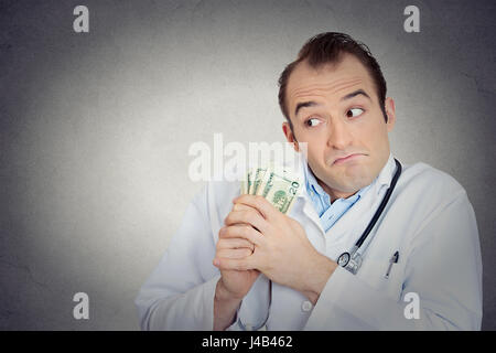 Closeup portrait avide avare grincheux professionnel de la santé, male doctor holding, protéger son argent dollars dans la main de mur gris isolé backgrou Banque D'Images