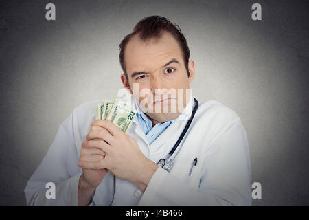 Closeup portrait avide avare grincheux professionnel de la santé, male doctor holding, protéger son argent dollars dans la main de mur gris isolé backgrou Banque D'Images