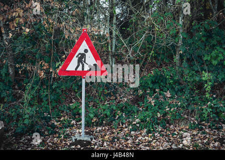 En construction inscrivez-vous avec un travailleur de creuser avec une pelle sur un panneau rouge dans une forêt verte Banque D'Images