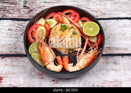 Poêlée de riz au jasmin avec de grandes crevettes roses en forme de coeur surmonté tranches de concombre,tomate et citron vert servi sur plat noir Banque D'Images