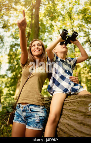 Beau jeune famille s'amuser dans la forêt. Petite fille à la découverte à travers des jumelles, sa mère avec le doigt pointant loin. Banque D'Images