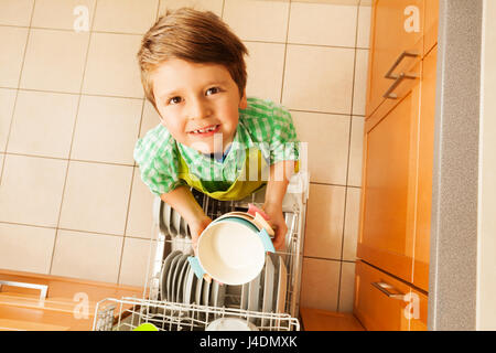 Cute boy holding bowls debout à côté d'un lave-vaisselle Banque D'Images