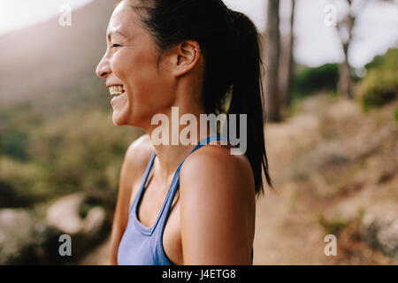 Vue de côté tourné de fit young woman standing outdoors, à l'écart et de rire. Happy female runner dans les vêtements de sport dans la matinée. Banque D'Images