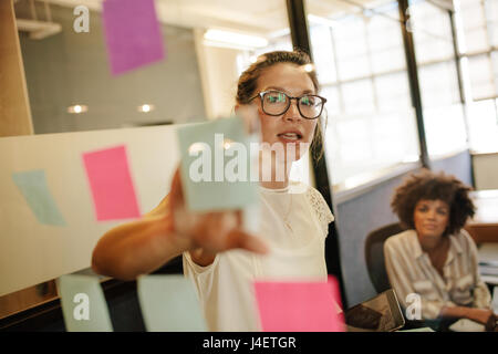 Business Woman pointing at sticky note à collègue sur mur en verre. Business projet ensemble. Banque D'Images