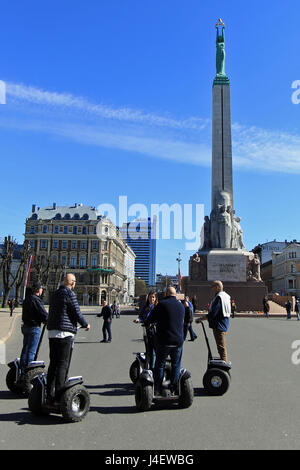 Les touristes en segways devant le monument de la liberté à Riga, Lettonie. Le Monument de la liberté est un monument situé à Riga, en Lettonie, en rendant hommage aux soldats tués pendant la guerre d'indépendance lettone (1918-1920). Il est considéré comme un important symbole de la liberté, l'indépendance et la souveraineté de la Lettonie. Dévoilé en 1935, les 42 mètres (138 pieds) de haut monument de granit, travertin, et souvent en cuivre est le point central de rassemblement public et des cérémonies officielles à Riga. Banque D'Images