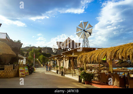 Bali, Grèce - 2 mai 2016 : moulin à vent décoratif avec hélice blanc installé sur un toit de chaume. Tables avec parasols en chaume à beach cafe sur seafr Banque D'Images