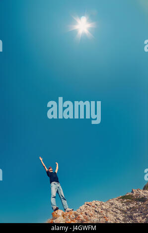 Jeune homme en jeans et chemise noire sur une montagne a levé la main au ciel vers le soleil. Concept de voyage photo verticale. Banque D'Images