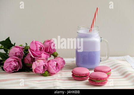 Café pourpre en pot Mason Tasse stylisée avec ses macarons et les roses et une décoration colorée. Lait frappé aux bleuets. Café Unicorn. L'alimentation Unicorn Banque D'Images