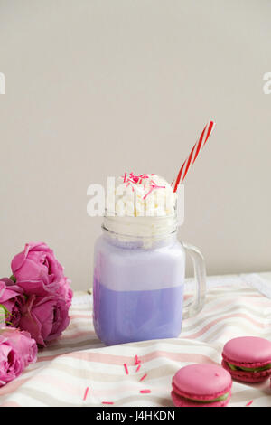 Café pourpre en pot Mason Tasse stylisée avec ses macarons et les roses et une décoration colorée. Lait frappé aux bleuets. Café Unicorn. L'alimentation Unicorn Banque D'Images