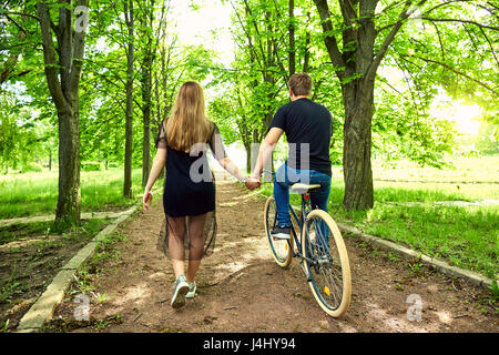 Un couple d'amoureux sur location détient les mains dans parc. Vue arrière Banque D'Images