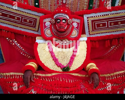 Artiste de l'art antique theatre Kathakali en costume et masque : rouge lumineux large vêtements, guirlande de fleurs rouges, masque rouge avec metal orbites, Keral Banque D'Images