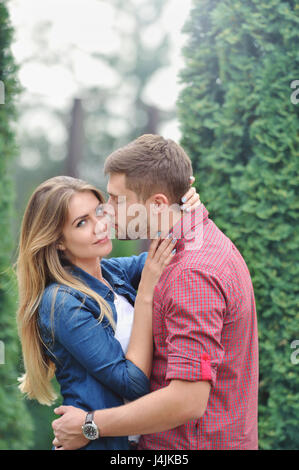 Jeune fille belle à regarder pendant que l'appareil photo d'être embrassé par son petit ami. L'amour, relation, famille et personnes concept - smiling couple hugging in Banque D'Images