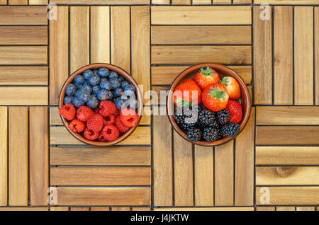 Vue de dessus de framboises, bleuets, fraises et des mûres dans un bol en terre cuite sur une surface en bois Banque D'Images