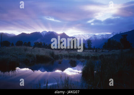 Nouvelle Zélande, île du sud, la saumure Matheson, prairie, arbres, montagnes, le coucher du soleil, l'eau du lac, la mise en miroir du soleil, crépuscule, crépuscule, ciel nuageux Banque D'Images